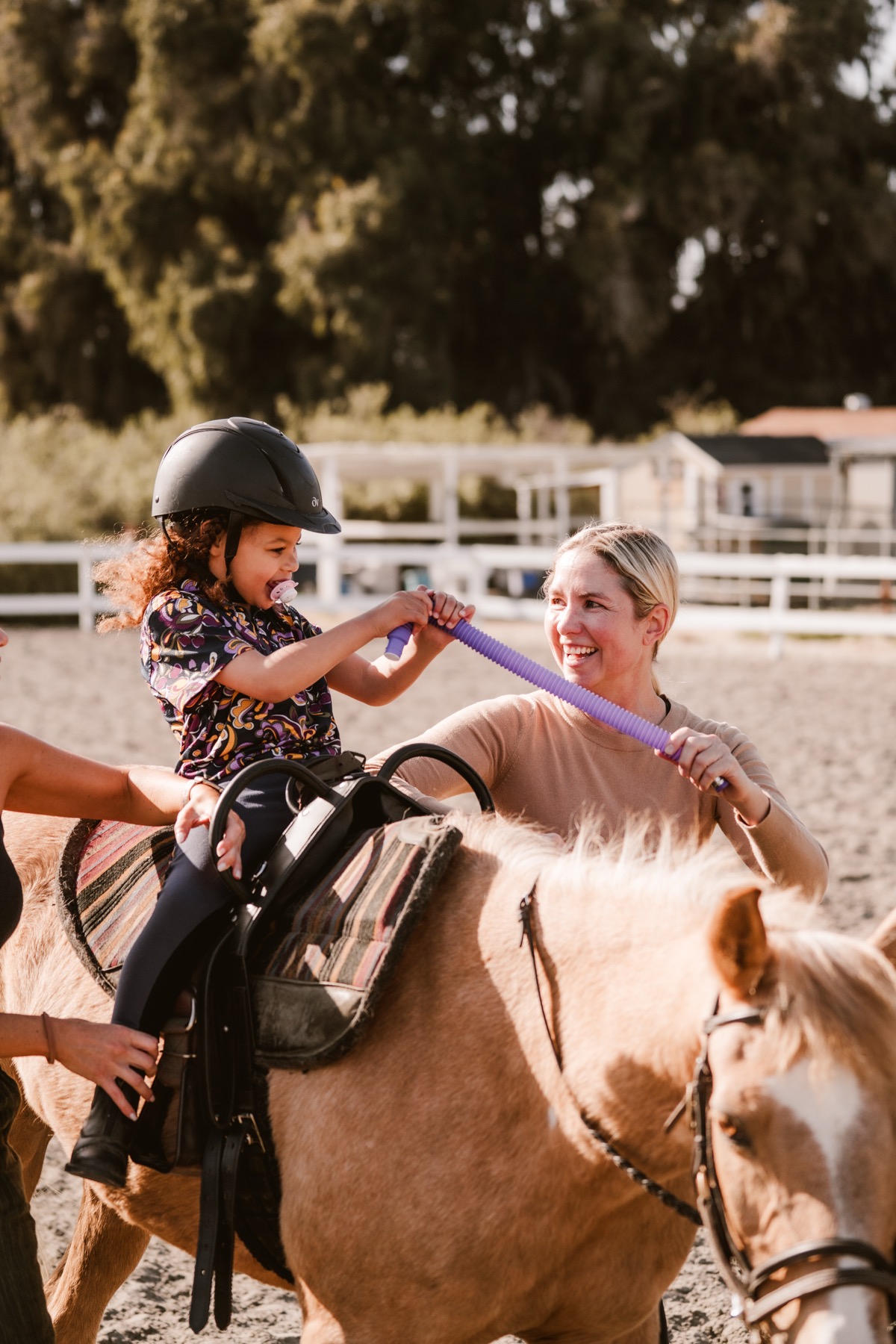 A laughing young rider on Melody stretches toward a smiling therapist during a session