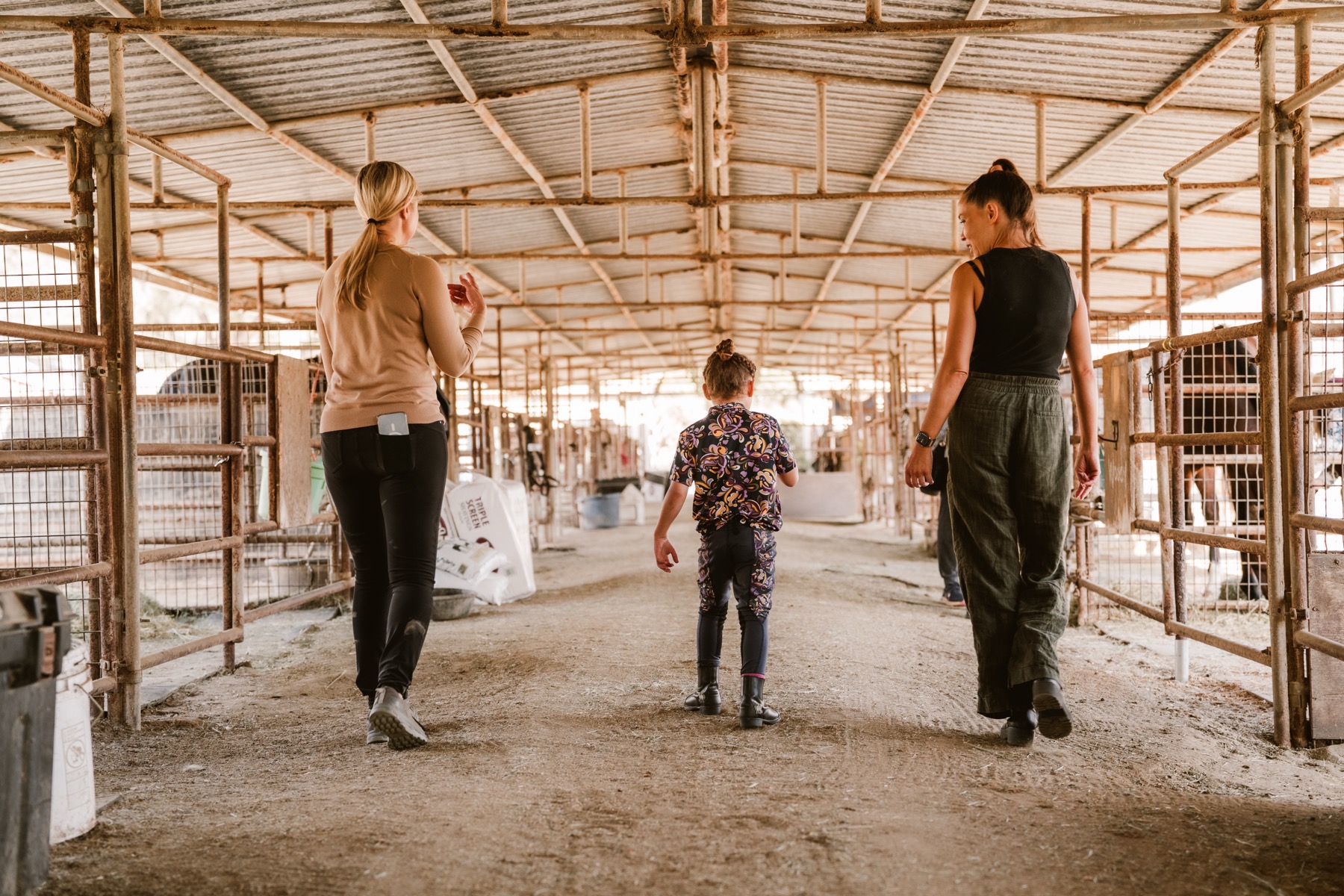 A volunteer and a child walk down the covered barn aisle lined with stalls