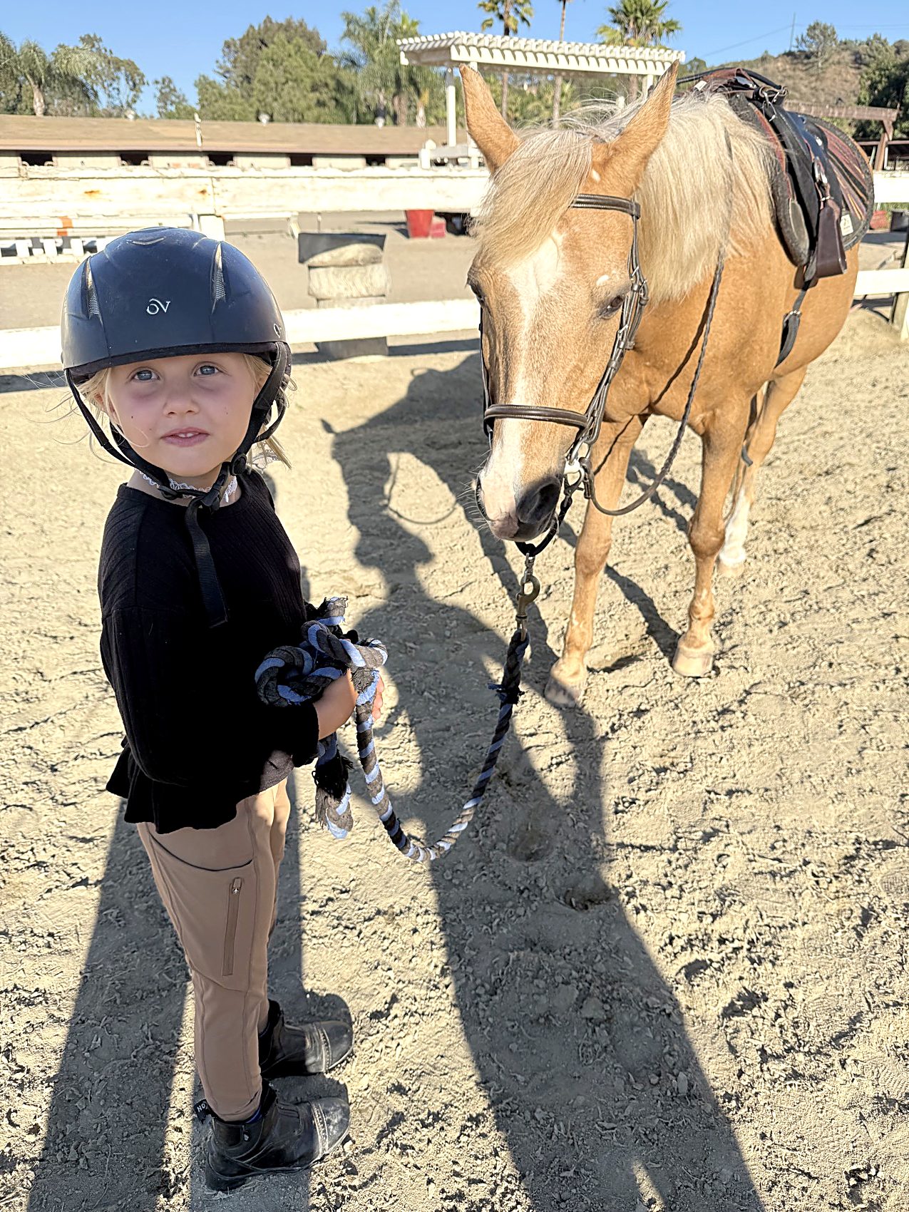 A young child in a riding helmet leads Melody by the rope