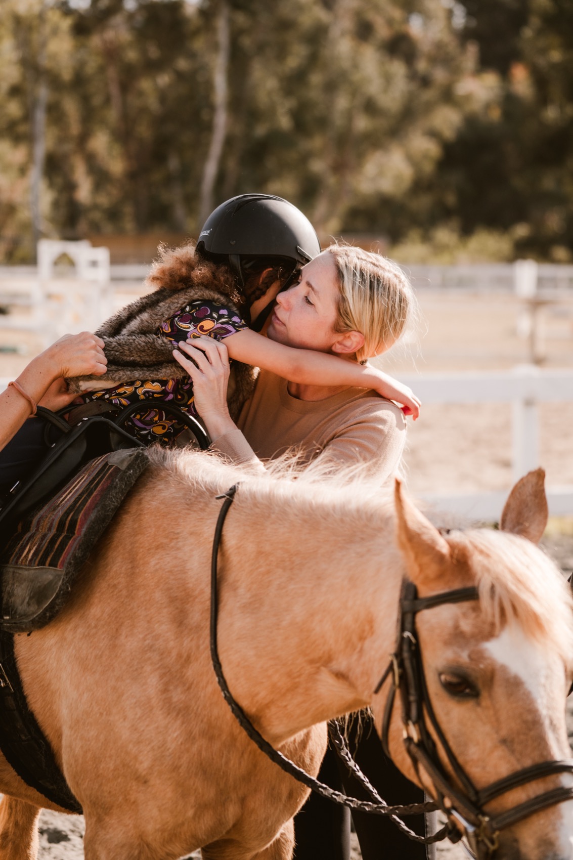 A therapist embraces a young rider mounted on Melody during a session