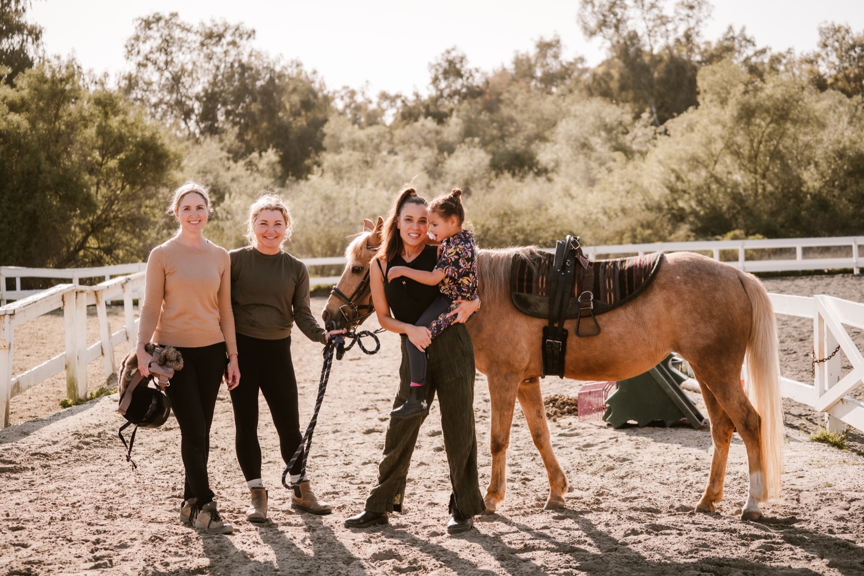 The Center X team and a young rider stand with Melody the palomino pony in the arena at golden hour
