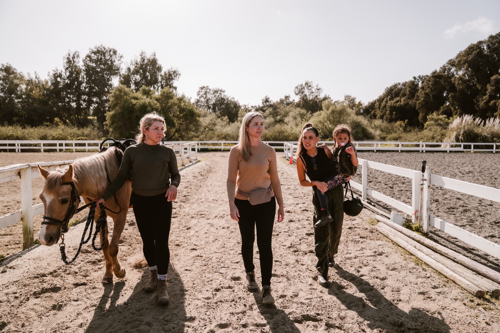 Volunteers and a child walk alongside the palomino pony across the sunny arena